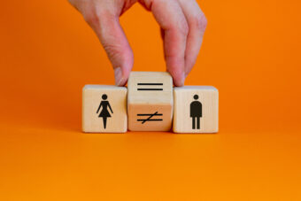 Trzy klocki drewniane na pomarańczowym tle. Pierwszy od lewej przedstawia postać kobiety, po prawej - mężczyznę. Między nimi jest ten, na którym znajduje się znak równości, zastępujący znak nierówności.