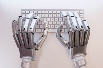 Ręce robota umieszczone na klawiaturze od komputera stacjonarnego.