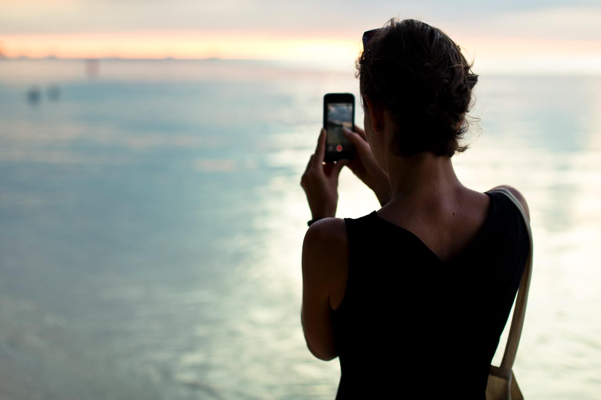 Kobieta robiąca zdjęcie telefonem, stojąca tyłem. 